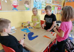 Dzieci na dużym arkuszu papieru malują rysunek farbami.