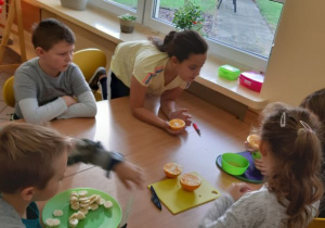 Owocowy zawrót głowy - kl.2a - dzieci kroją owoce przy stoliku.