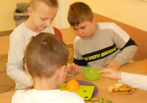 Owocowy zawrót głowy - kl.3b - dzieci kroją owoce przy stoliku.