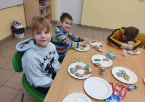 Uśmiechnięci chłopcy siedzą przy stole, na stoliku są talerzyki z ozdobionymi pierniczkami.