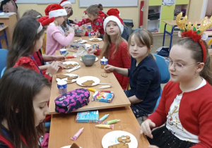 Dzieci siedzą przy stolikach i ozdabiają świąteczne pierniki.