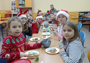 Dzieci siedzą przy stolikach i ozdabiają świąteczne pierniki.