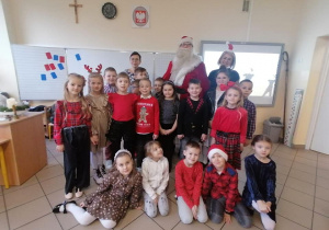 Zdjęcie grupowe dzieci z Mikołajem w sali lekcyjnej.