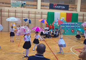 Dzieci wykonują układ taneczny z parasolkami na sali gimnastycznej.