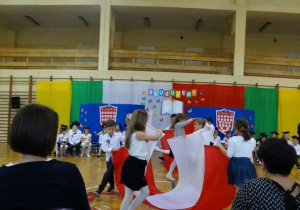 Pierwszoklasiści wykonują Taniec z Flagą na sali gimnastycznej podczas części artystycznej poprzedzającej ślubowanie